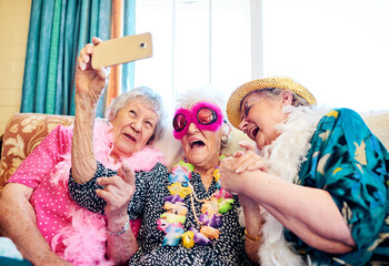 How does this thing work. Shot of a group carefree elderly people wearing funky costumes and getting close for a selfie inside of a building.