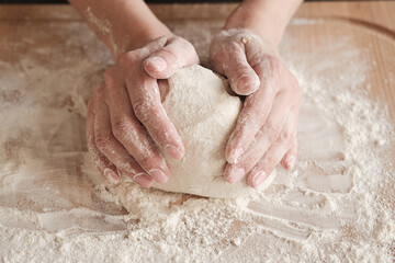 Close-up of unrecognizable woman touching dough ball on board with flour while kneading