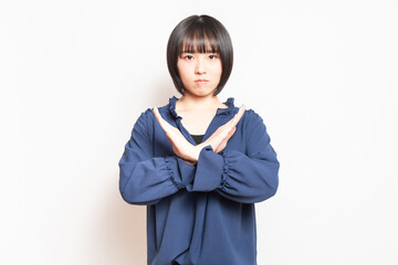 白い壁の前に立ってNGのジェスチャーをする若い女性