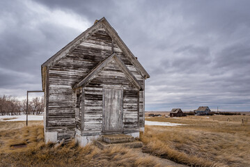 The exterior of an abandoned schoolhouse with  two abandoned homes in the background on the...