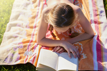 Get lost in a good piece of literature. Shot of a teenage girl lying on a towel while reading a book.
