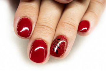 Red gel polish on female fingernails. Painted black floral decorations, golden foil, neat manicure. Selective focus on the details, blurred background.