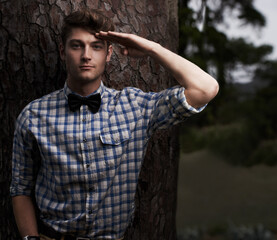 Heres to you. Portrait of a handsome young man saluting the camera while standing outside in front of a tree.