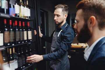 Man sommelier helps visitors to restaurant or liquor store to choose bottle of wine