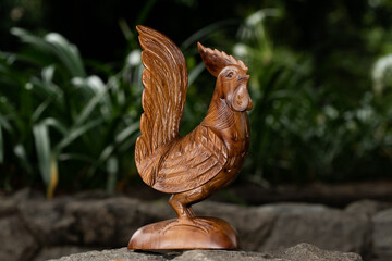 Wooden statue of a rooster on a green plant background.