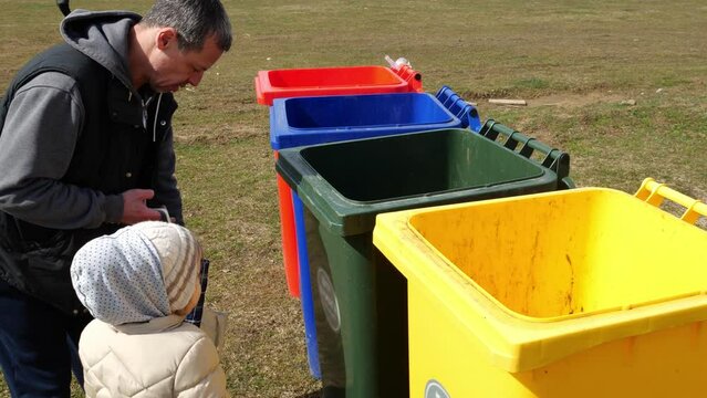 Different color recycle bin containers. Glass plastic metal cans paper waste recycling. Dad teaches daughter to sort household waste