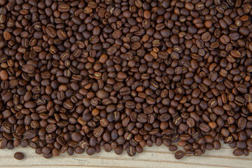Roasted coffee beans on a light brown wooden floor.