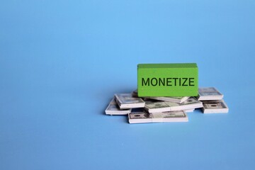 Wooden cube with text MONETIZE and banknotes on blue background. Business and financial concept.