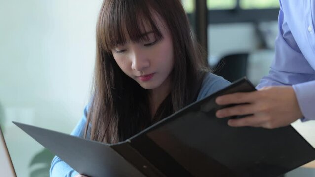Young Asian business partners reading document and discussing plans or ideas at meeting, Consultant or explainer concept