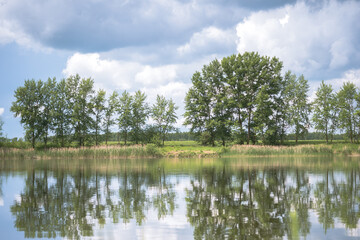 Fototapeta na wymiar Spring landscape of the lake with trees in bright greenery and a picturesque sky in cumulus clouds. Background