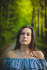 Breathtaking candid portrait of a young brunette in a beautiful summer blue dress on a forest path surrounded by lush summer trees. A measured and ambitious look