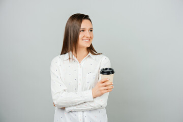 Young smiling woman looking away is holding a take away cup of coffee.