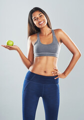 What they say about an apple a day is true. Cropped studio portrait of an attractive young woman holding an apple against a gray background.