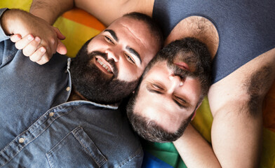 Young male couple lying together on flag with rainbow colors. Concept of pride of gay men and lgbt...