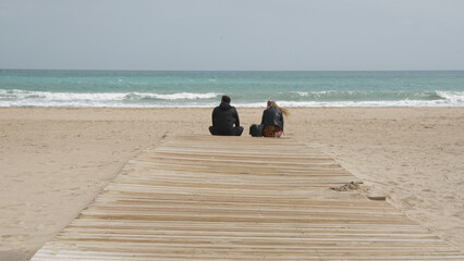 Pareja primera cita sentados en la playa frente al mar