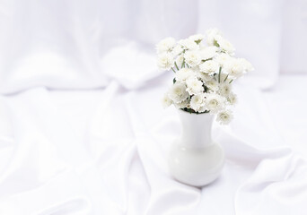 White flowers in white vase on white background with copy space and selective focus. Greeting or invitation card