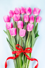 Fototapeta premium Bunch of beautiful pink white tulips tied with red ribbon on blue background, vertical, top view