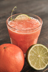 Close-up of refreshing grapefruit juice decorated with lime slice and twig on wooden table with citrus fruits