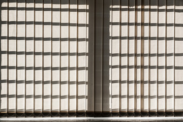 Dense shutter hanging on big window is closed. Protection from sun light at room.
