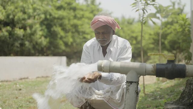 Happy Indian farmer after seeing water on borewell pipe at farmland - cocnept of happiness, poverty and water for agricultural works
