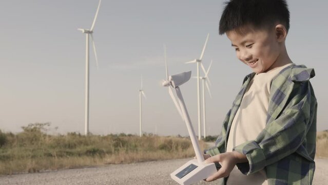 Happy Asian kid with toy windmill in hand at wind farm, Renewable energy concept