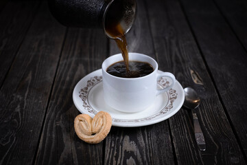 pouring black espresso coffee from coffee maker into white cup wooden background