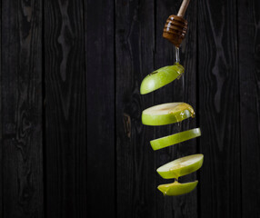 Levitation of a green apple with drops of amber honey on a dark wooden background, copy space
