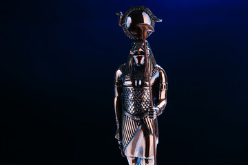 metal statue of the Egyptian god Ra with the head of a falcon on a black background with blue...