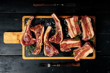 Raw T-bone steak and ribs on a black stone cutting board. Raw meat with spices and herbs. Top view. Dark wooden background. Copy space