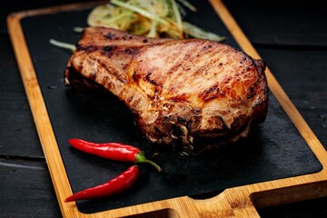 Grilled meat on a stone board. Appetizing grilled steak with herbs and spices. Dark wooden background