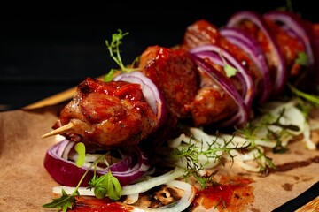 Kebabs. Appetizing grilled meat with vegetables and herbs on a black wooden background. Soft focus. Close up