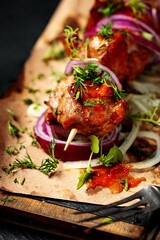 Kebabs. Appetizing grilled meat with vegetables and herbs with spicy sauce on a black wooden background. Soft focus. Vertical shot