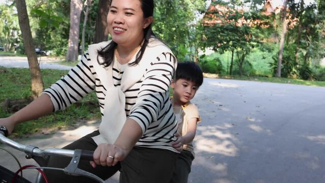 Asian Mother ride a bicycle with son and having fun together in the garden, Parents activity with kid concept