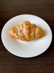 large vertical photo. view from above. white porcelain plate with an almond croissant in the center. close-up. breakfast. homemade baking.