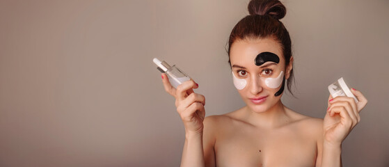 Obraz premium A young woman with care cosmetics in her hands cannot make a choice. She has a lot of patches on her face, black and white, serum and cream in her hands.