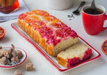 A whole cake with blood oranges on top on a white rectangular plate on a light concrete background.