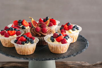 Fruit cakes on black stone stand. Muffins decorated with fresh berries. Homemade cupcake on gray background