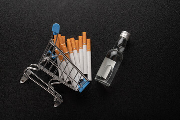 Small grocery cart with cigarettes and bottle of alcohol on back background. Top view. Purchase of...