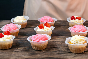 Cupcakes with cream and strawberries. Homemade vanilla muffins on wooden table.
