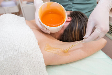 A beautician makes a sugar paste depilation under the armpits in a beauty salon.