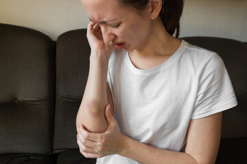 Suffering young woman in white t-shirt with large bruise on arm. Victim of domestic violence.