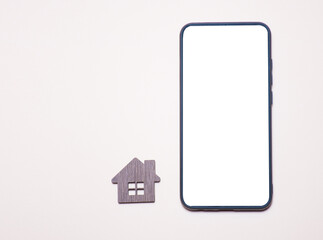 Mobile phone with a cut-out place for text on a monochrome background next to a wooden model of a house: real estate services, real estate purchase, home design projects, online consultations