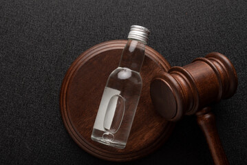Law hammer and bottle of alcohol on black background top view. Alcohol legislation.