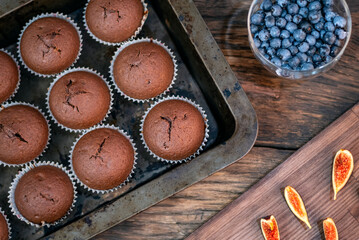 Flat lay cupcakes in bakeware, figs and berries on wooden table. Homemade muffins.