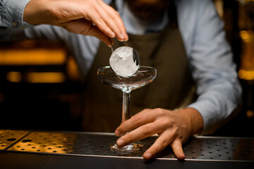 view on round piece of ice held by tongs in male hand over transparent wine glass