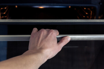 The hand opens the oven door. 