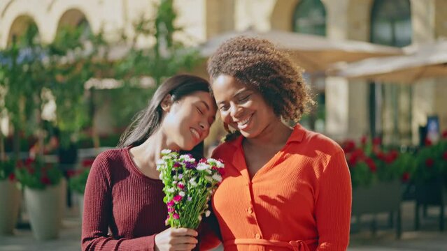 Cheerful lesbian couple walking on date with bouquet of flowers, relationship