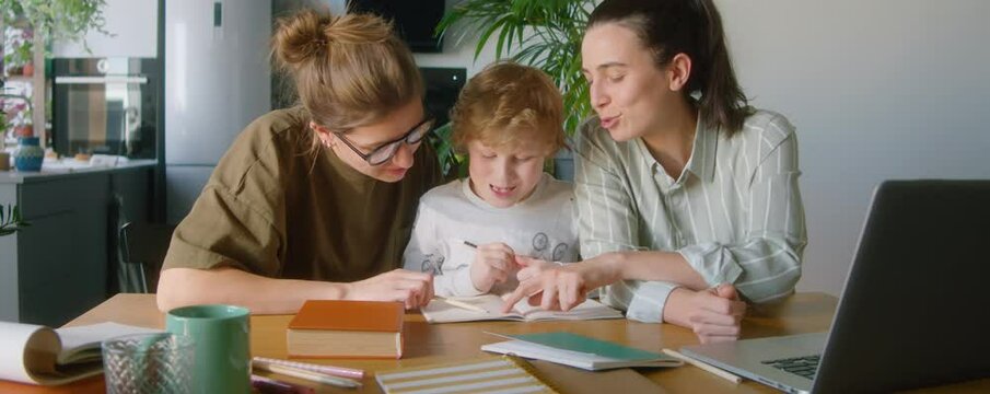 Little boy talking with lesbian mothers and taking notes in workbook while studying at home