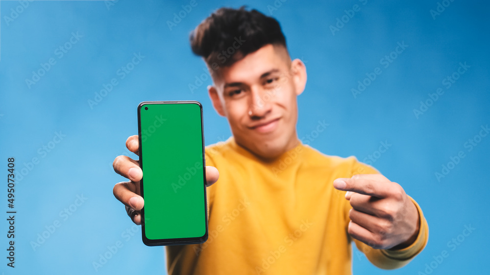 Poster man pointing to a mobile phone with green screen while standing on an isolated background.