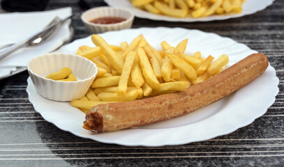 German Bratwurst or grilled sausage with French fries, mustard and ketchup on a plate in a street restaurant, unhealthy fast food, selected focus